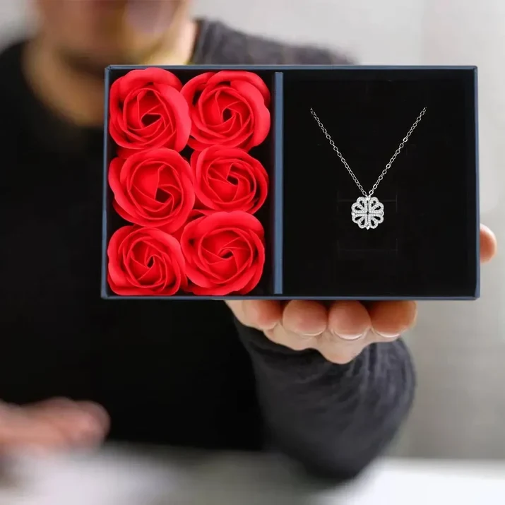 The necklace in its midnight-blue gift box beside six red preserved roses